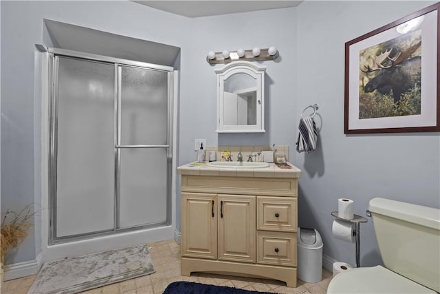 bathroom featuring toilet, vanity, baseboards, and a stall shower