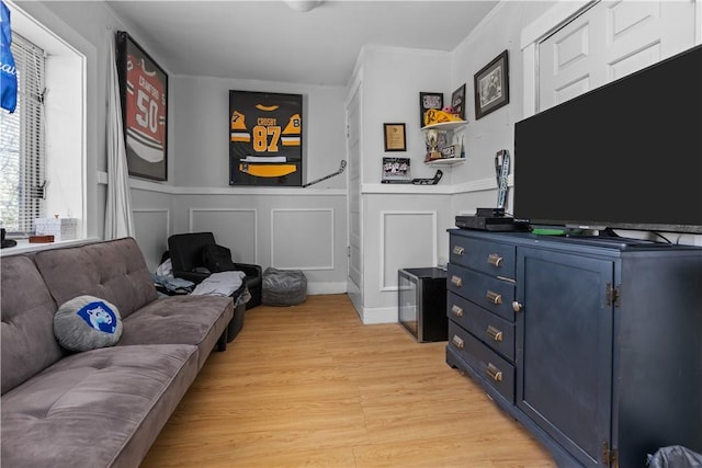 living area with a decorative wall, light wood-style flooring, a wainscoted wall, and crown molding
