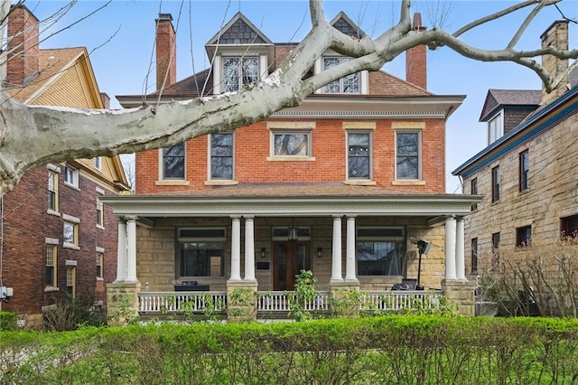 view of front of house with brick siding, a porch, stone siding, and a chimney