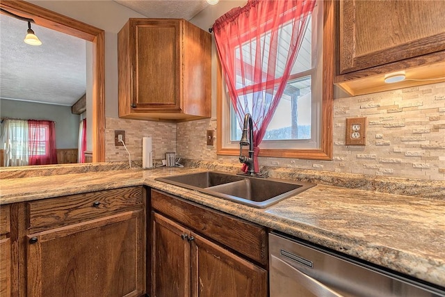 kitchen featuring tasteful backsplash, a textured ceiling, brown cabinets, dishwasher, and a sink