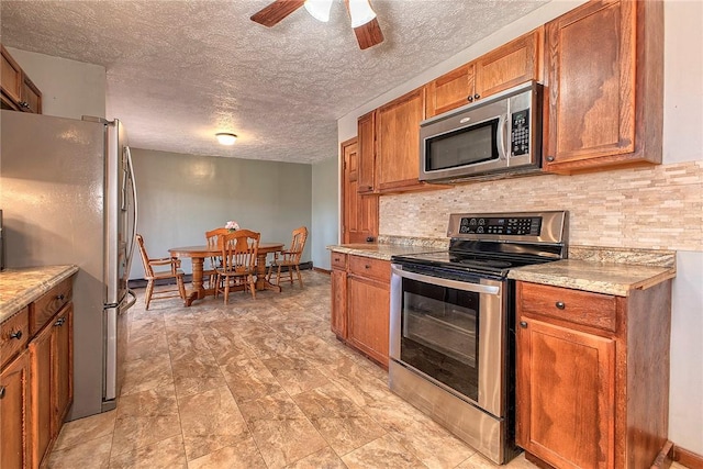 kitchen featuring tasteful backsplash, a textured ceiling, a ceiling fan, brown cabinets, and appliances with stainless steel finishes