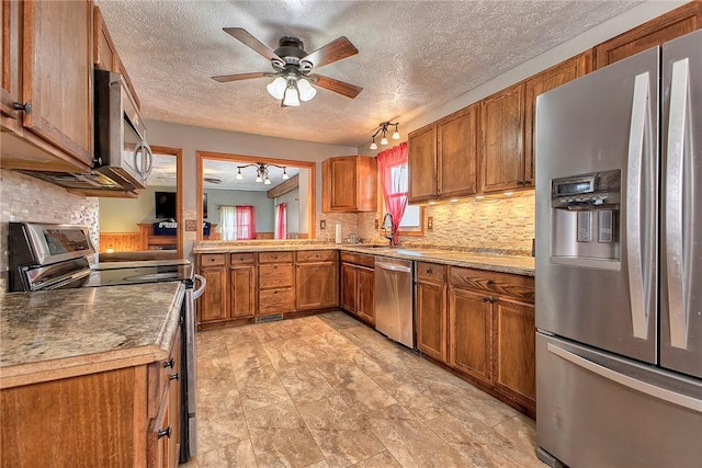 kitchen with a sink, brown cabinetry, ceiling fan, and stainless steel appliances