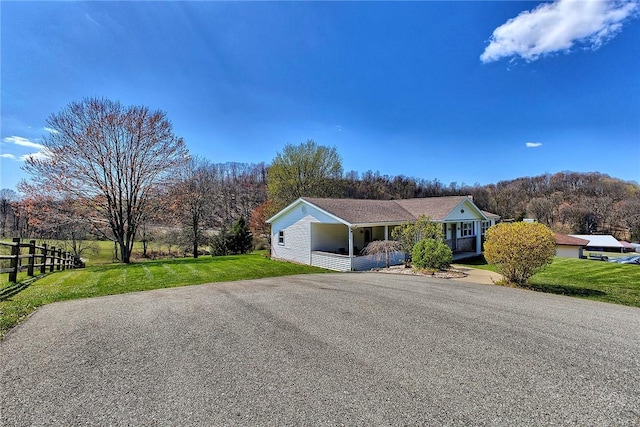 ranch-style house featuring a porch, driveway, fence, and a front lawn