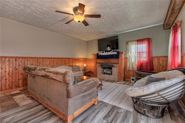 living room featuring a ceiling fan, a textured ceiling, wood finished floors, wood walls, and a wainscoted wall