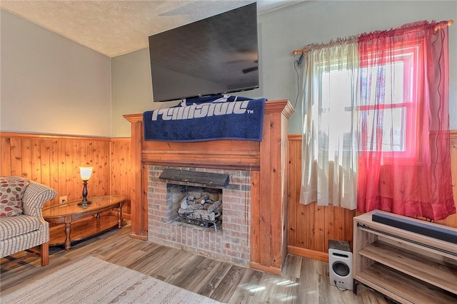 living area with wooden walls, a wainscoted wall, a brick fireplace, and wood finished floors