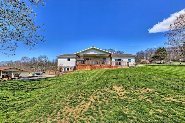 rear view of house with a yard, a wooden deck, and fence