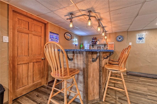 bar featuring a bar, a textured wall, a paneled ceiling, and wood finished floors