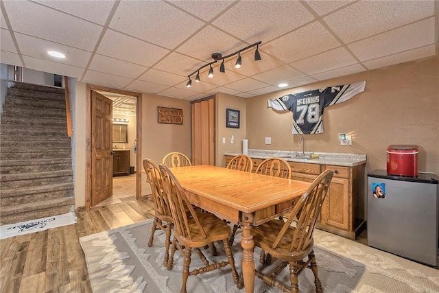 dining room featuring light wood-type flooring, a paneled ceiling, wet bar, and stairway