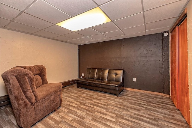 living area featuring a textured wall, baseboards, a drop ceiling, and wood finished floors
