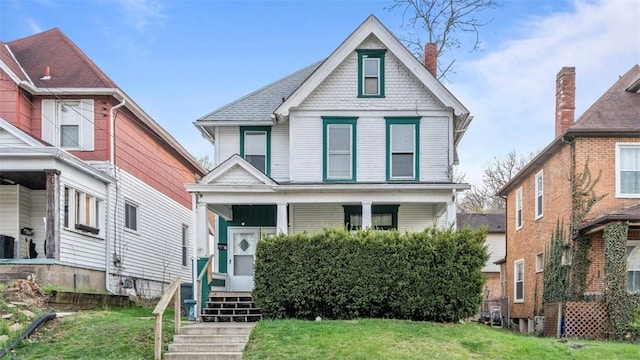 view of front of home with a chimney, covered porch, and a front yard