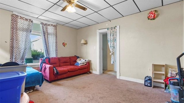 living area with ceiling fan, a drop ceiling, carpet, and baseboards