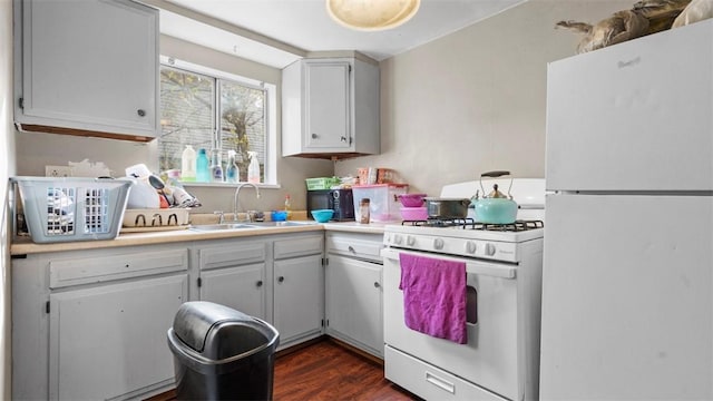 kitchen with a sink, light countertops, white appliances, and dark wood finished floors