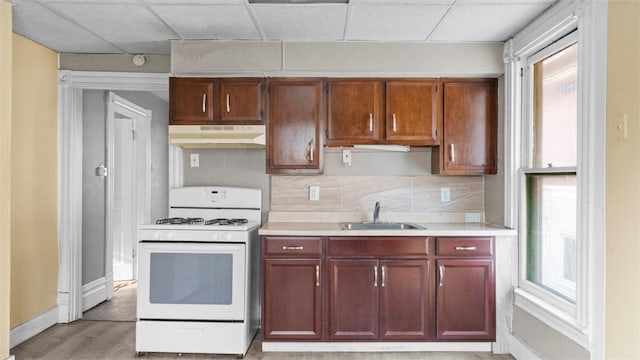 kitchen with white gas stove, under cabinet range hood, a sink, and a healthy amount of sunlight