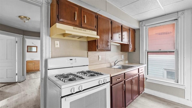 kitchen featuring light wood-style flooring, light countertops, white gas range, under cabinet range hood, and a sink