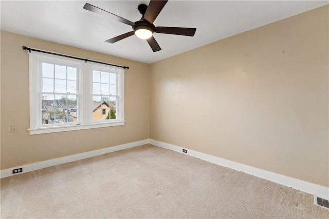 empty room with ceiling fan, light colored carpet, baseboards, and visible vents