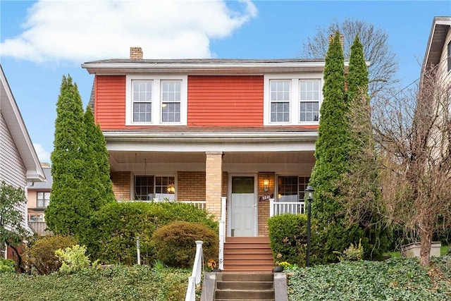 view of front facade featuring a porch, a chimney, and brick siding