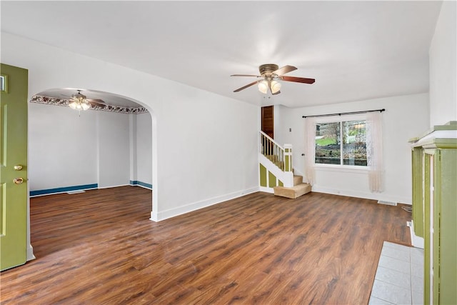 unfurnished living room featuring arched walkways, stairway, a ceiling fan, and wood finished floors