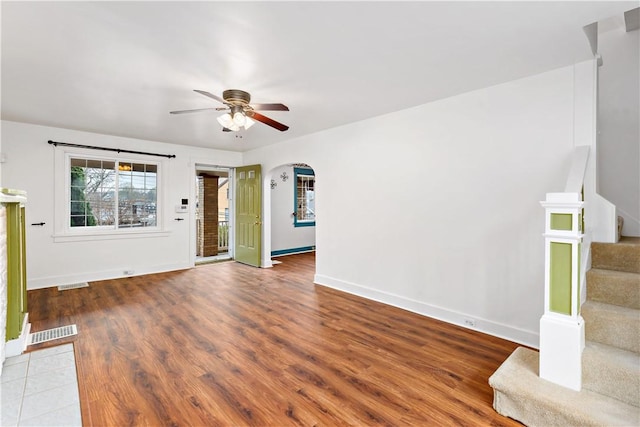 unfurnished living room with baseboards, a ceiling fan, stairs, visible vents, and arched walkways