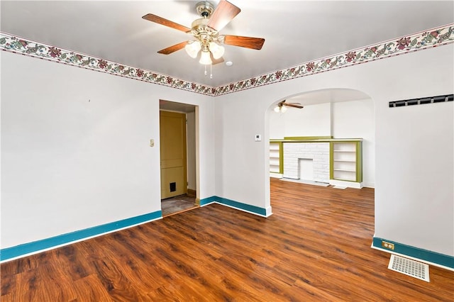unfurnished room featuring baseboards, a ceiling fan, visible vents, arched walkways, and wood finished floors