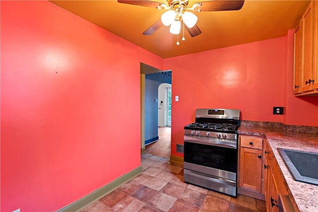 kitchen with arched walkways, a ceiling fan, gas stove, a sink, and baseboards