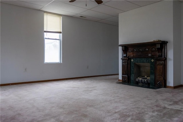 unfurnished living room with baseboards, a tiled fireplace, a ceiling fan, a paneled ceiling, and carpet floors