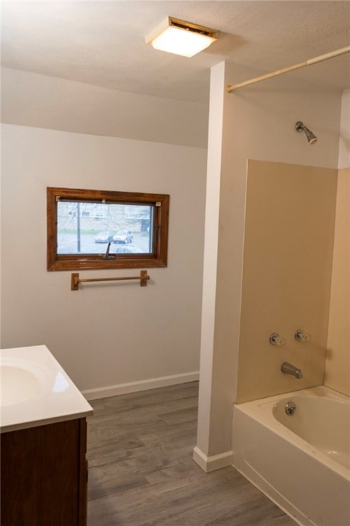 bathroom with baseboards, wood finished floors, vanity, and shower / washtub combination