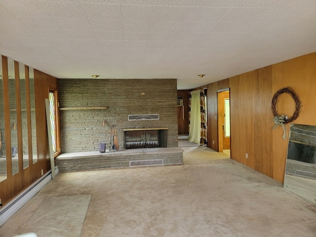 unfurnished living room with a brick fireplace, a baseboard heating unit, carpet flooring, and wooden walls