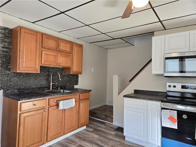 kitchen featuring a sink, light wood-type flooring, appliances with stainless steel finishes, backsplash, and a drop ceiling