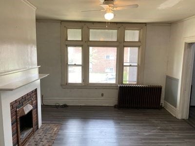 140 Washington Ave, Bellevue, PA 15202 - unfurnished living room featuring radiator, ceiling fan, a fireplace, wood finished floors, and baseboards