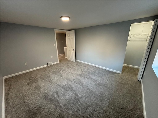 unfurnished bedroom with a closet, a spacious closet, visible vents, carpet floors, and baseboards