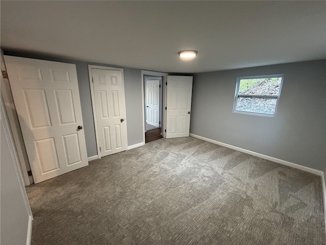 unfurnished bedroom with dark carpet and baseboards
