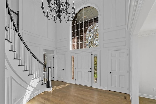 foyer with an inviting chandelier, a decorative wall, stairs, wood finished floors, and a towering ceiling