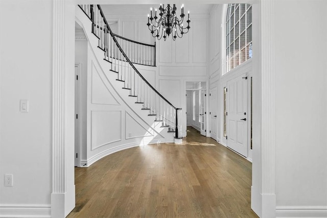 entrance foyer with stairs, a towering ceiling, wood finished floors, and a decorative wall