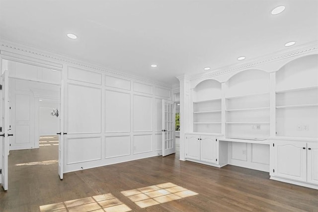 unfurnished living room with crown molding, dark wood finished floors, built in shelves, and a decorative wall