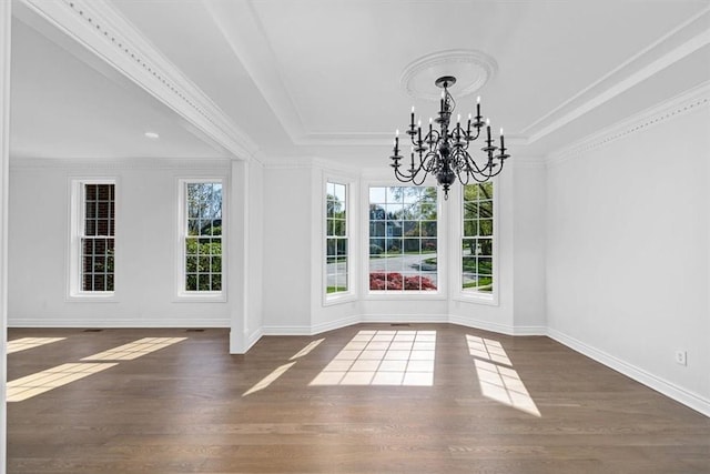 unfurnished dining area featuring a chandelier, baseboards, wood finished floors, a tray ceiling, and ornamental molding