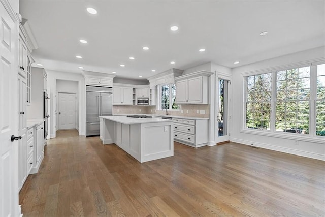 kitchen with light countertops, built in appliances, a kitchen island, and wood finished floors