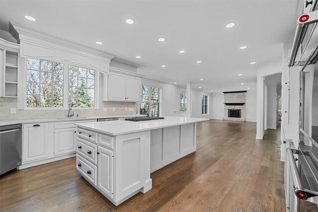 kitchen featuring a center island, dishwasher, a sink, light countertops, and white cabinets