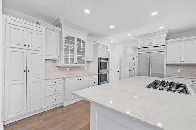 kitchen featuring appliances with stainless steel finishes, recessed lighting, white cabinetry, light wood-type flooring, and glass insert cabinets