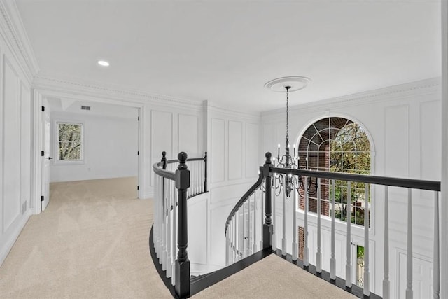 hallway with crown molding, an upstairs landing, a chandelier, light carpet, and a decorative wall