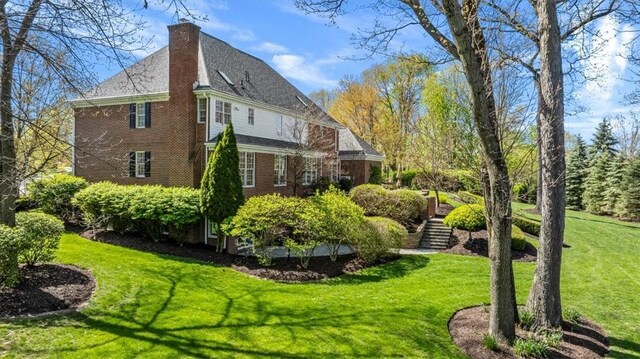 view of side of home featuring a chimney, a yard, stairway, and brick siding