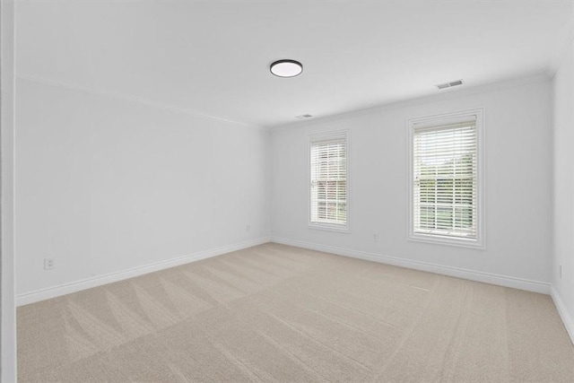 empty room featuring carpet floors, ornamental molding, baseboards, and visible vents