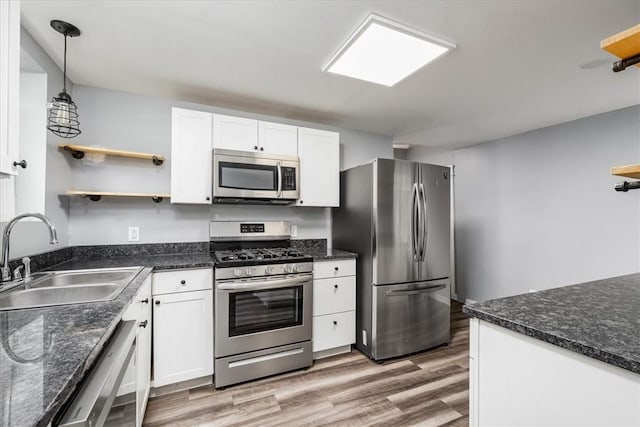 kitchen with white cabinets, a sink, light wood-style floors, stainless steel appliances, and pendant lighting