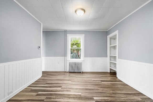 unfurnished room featuring ornamental molding, radiator heating unit, wood finished floors, and a wainscoted wall