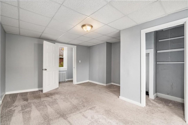unfurnished bedroom with a closet, baseboards, radiator, carpet, and a drop ceiling
