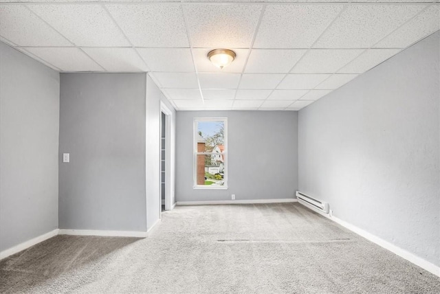 carpeted empty room featuring baseboard heating, a paneled ceiling, and baseboards