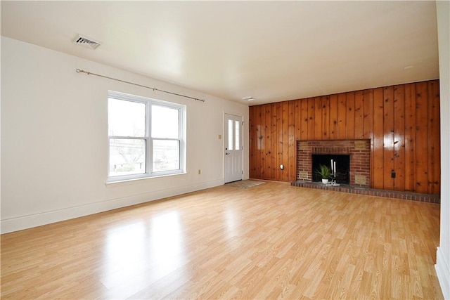 unfurnished living room featuring light wood-style flooring, visible vents, wood walls, a brick fireplace, and baseboards