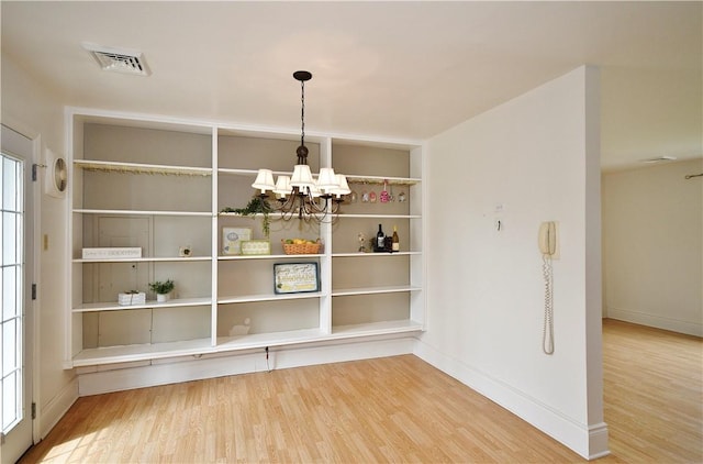 unfurnished dining area with visible vents, baseboards, an inviting chandelier, and wood finished floors