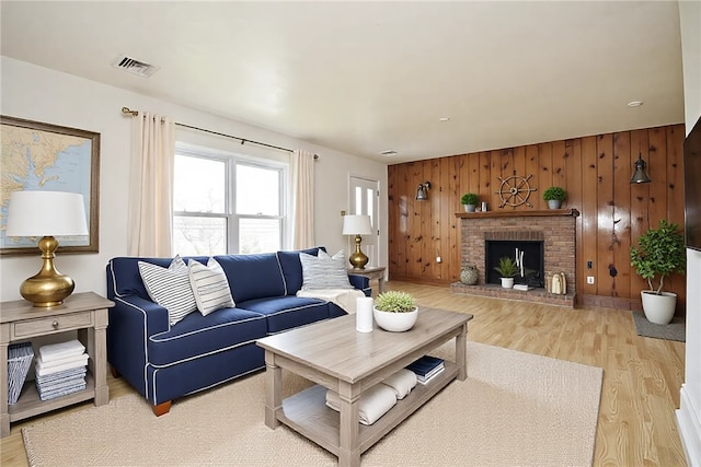 living room featuring wood walls, visible vents, light wood-type flooring, and a brick fireplace