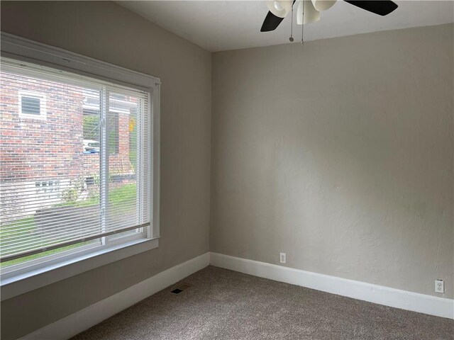 carpeted empty room with visible vents, baseboards, a ceiling fan, and a healthy amount of sunlight