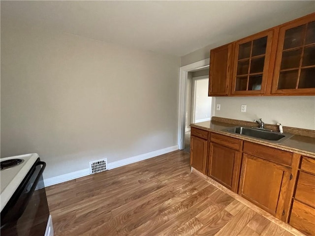 kitchen featuring light wood-type flooring, visible vents, a sink, white electric stove, and brown cabinets